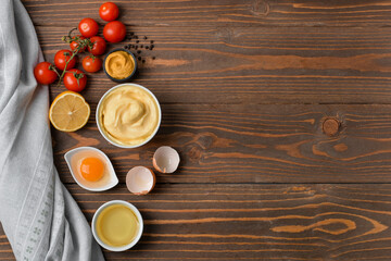 Bowl with tasty mayonnaise sauce and ingredients on wooden background