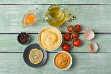 Bowl with tasty mayonnaise sauce and ingredients on green wooden background