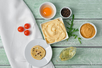Bowl with tasty mayonnaise sauce and ingredients on green wooden background
