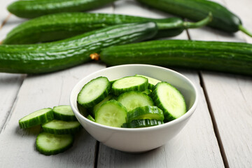 Bowl with fresh cut cucumber on light wooden background