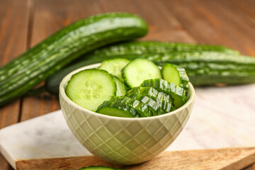 Bowl with fresh cut cucumber on wooden background, closeup