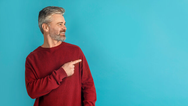 Handsome middle aged man pointing at copy spaceon blue