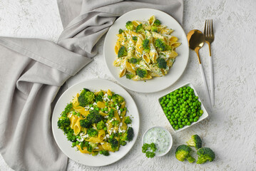 Plates with tasty pasta and broccoli on light grunge background