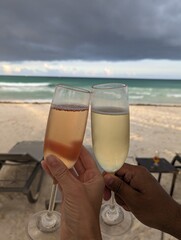 Hand of a couple holding champagne glasses at beach in front of storm sky