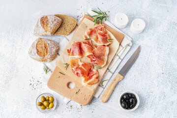 Wooden board with slices of tasty jamon on light background