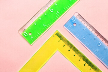 Colorful straight and triangle plastic rulers on pink background