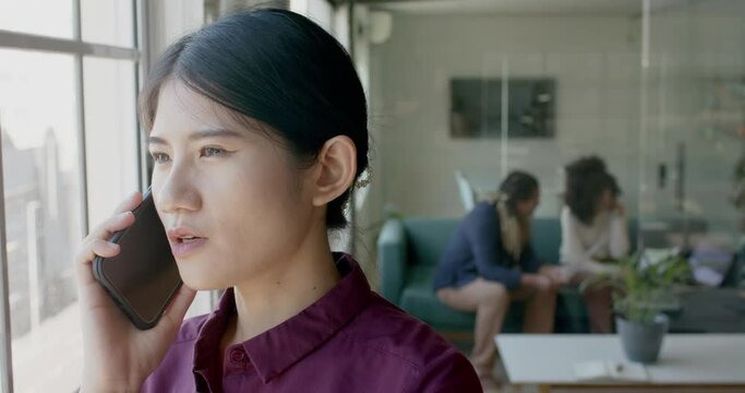 Busy asian casual businesswoman talking on smartphone in creative office, slow motion