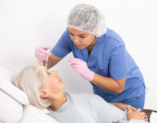 Serious aged woman having mesotherapy procedure by injection on her face conducted by dermatologist