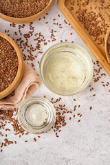 Glass and bowl with flax oil and seeds on light background