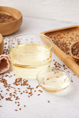Glass and bowl with flax oil and seeds on light background