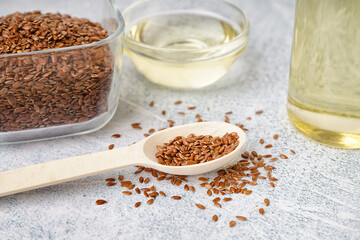 Spoon with flax seeds and bowl of oil on light grunge background