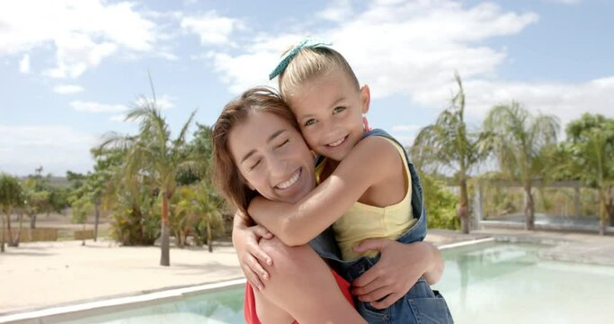 Portrait of happy caucasian mother carrying daughter at swimming pool at beach house