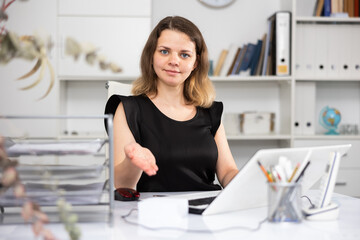 Portrait of female manager sitting at her desktop in office and making palm gesture.