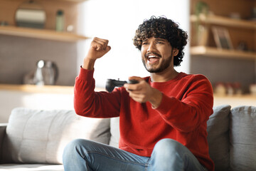 Cheerful Young Indian Guy Celebrating Win While Playing Video Games At Home