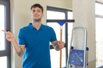 young handsome man smiling cheerfully, feeling happy and pointing to the side. windows washer...