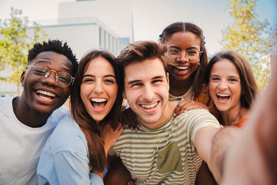 Happy multicultural friends laughing taking a selfie portrait together. Mixed teenage cheerful students having fun and hanging out. Young multiracial joyful people looking at camera and bonding . High