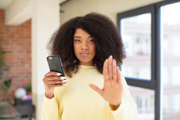 Obraz na płótnie Canvas pretty afro black woman looking serious showing open palm making stop gesture. smartphone concept