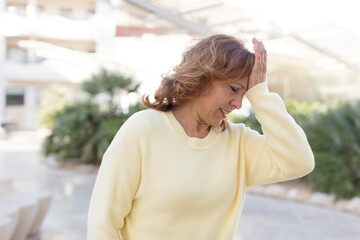 middle age woman laughing and slapping forehead like saying d’oh! I forgot or that was a stupid...