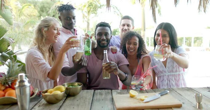 Portrait of happy diverse group of friends talking and drinking drinks at beach bar