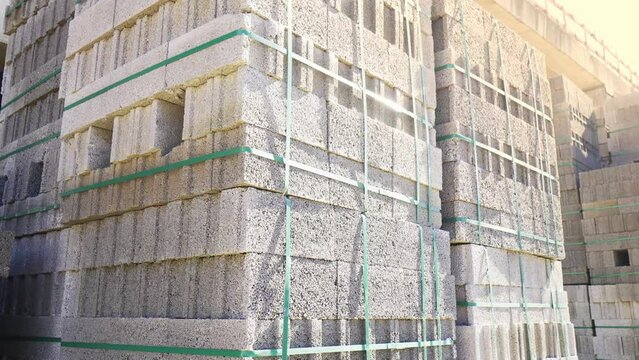 Large stack of pumice blocks and blocks packed on pallets in form of cube. Construction site, camera moving, large number of blocks against background of construction and sunlight.
