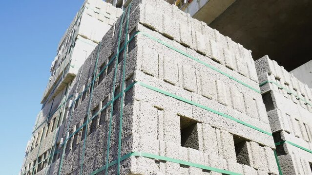 Large stack of pumice blocks and blocks packed on pallets in form of cube. Construction site, camera moving, large number of blocks against background of construction and sunlight.