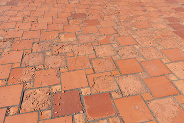 Rote quadratische Bodenplatten, die durch Witterungseinflüsse oder Materialfehler beschädigt sind. Die Oberfläche zerbröselt und die Platten lösen sich auf. 