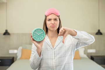 young pretty woman feeling cross,showing thumbs down. alarm clock concept