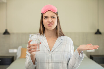 young pretty woman shrugging, feeling confused and uncertain. water glass concept