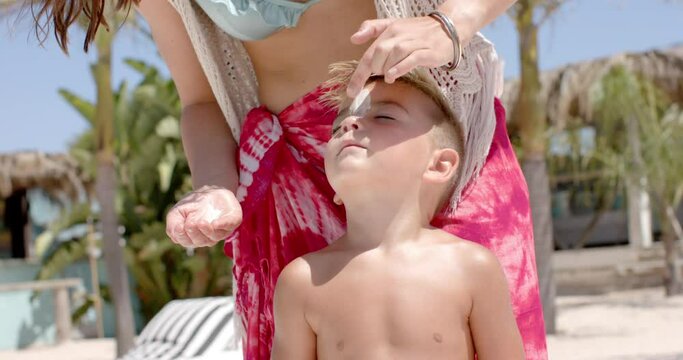 Happy caucasian mother using suncream on her son at swimming pool