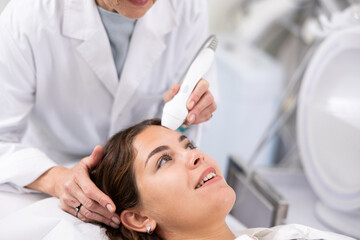 Careful aged woman doctor conducting laser therapy of young woman patient's face in aesthetic clinic