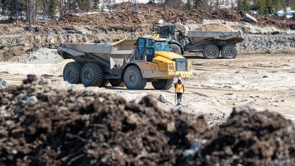 Dumpers driving on a construction site and a surveyor on a sunny day