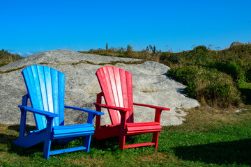 Bright red and blue empty sturdy resin material Adirondack chairs. The furniture is on green lush...