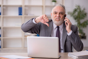 Old male employee speaking by phone at workplace