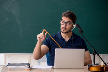 Young male music teacher sitting in the classroom
