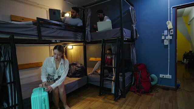 4K Man and woman traveler with luggage walking into shared bedroom in hostel. Small business lower-priced inn service with shared accommodations and bunk beds for backpacker tourist on travel trip.