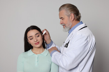 Doctor dripping medication into woman's ear on light grey background