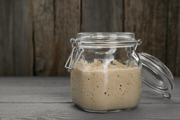 Leaven in glass jar on grey wooden table, space for text