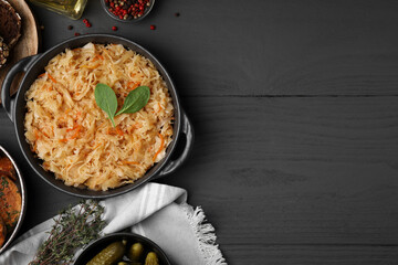 Serving pan with sauerkraut and products on black wooden table, flat lay. Space for text