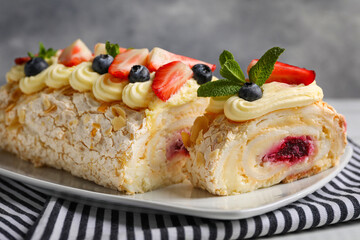 Tasty meringue roll with jam, cream, strawberry, blueberry and mint on plate, closeup