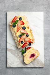 Tasty meringue roll with jam, cream, strawberry, blueberry and mint on light grey table, top view