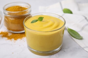 Tasty curry sauce, powder and basil leaves on white table, closeup