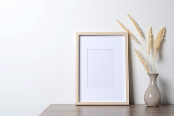 Empty photo frame and vase with dry decorative spikes on wooden table. Mockup for design