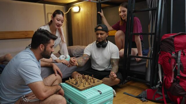 Group of Diversity traveler people spend time together playing chess in shared bedroom at hostel. New friends meeting in shared accommodations. Tourist resting in low price inn on travel vacation trip