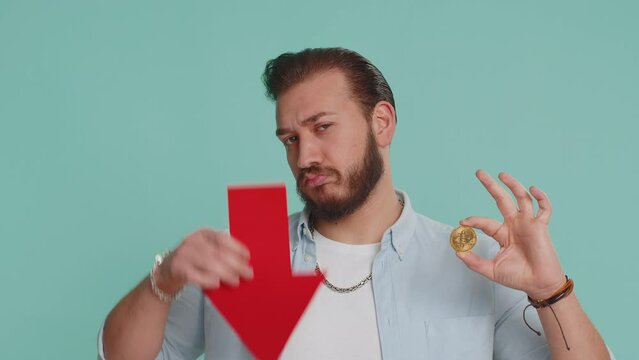 Upset lebanese man showing red arrow pointing down downgrade, unsuccessful business fall of cryptocurrency stock market investment, mining bitcoins BTC money exchange rate bankruptcy fail. Arabian guy
