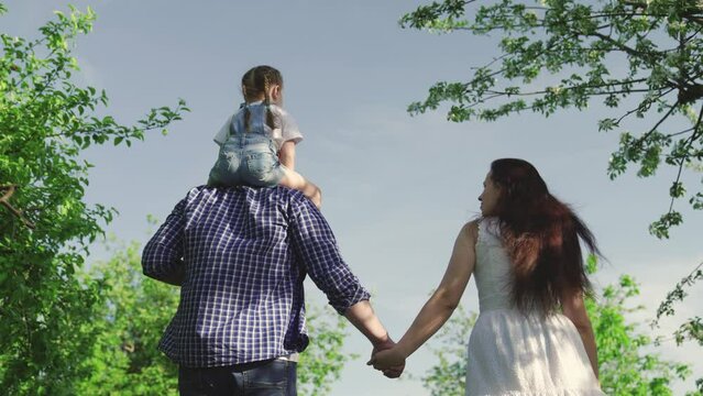 Kid girl plays with father mother. Happy family go in park holding hands in summer. Dad little daughter Mom playing together, holiday in spring. Happy child hugs dad with his hands. Kid mom dad walk