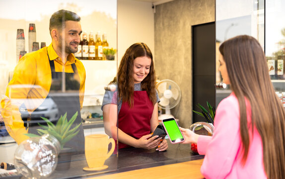 Happy waiter with a client at the cafe or ice-cream shop, making contactless payment with a smartphone - Powered by Adobe