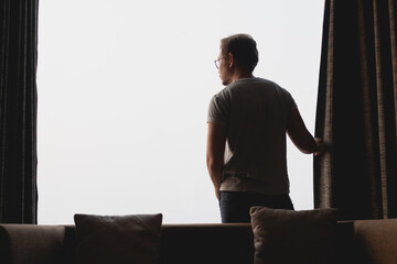 Asian man closing the curtain while watching the view out of the window.