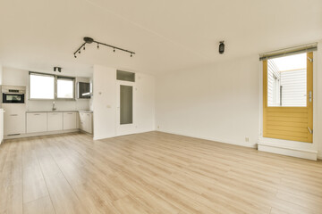 an empty living room with wood flooring and yellow door leading to the kitchen in the room is very clean