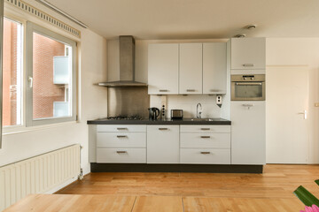 a kitchen with white cabinets and wood flooring in the middle of the room, looking out to the outside