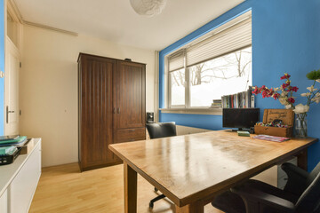 a dining room with blue walls and wood flooring in the center of the room is a wooden table, black chairs and a